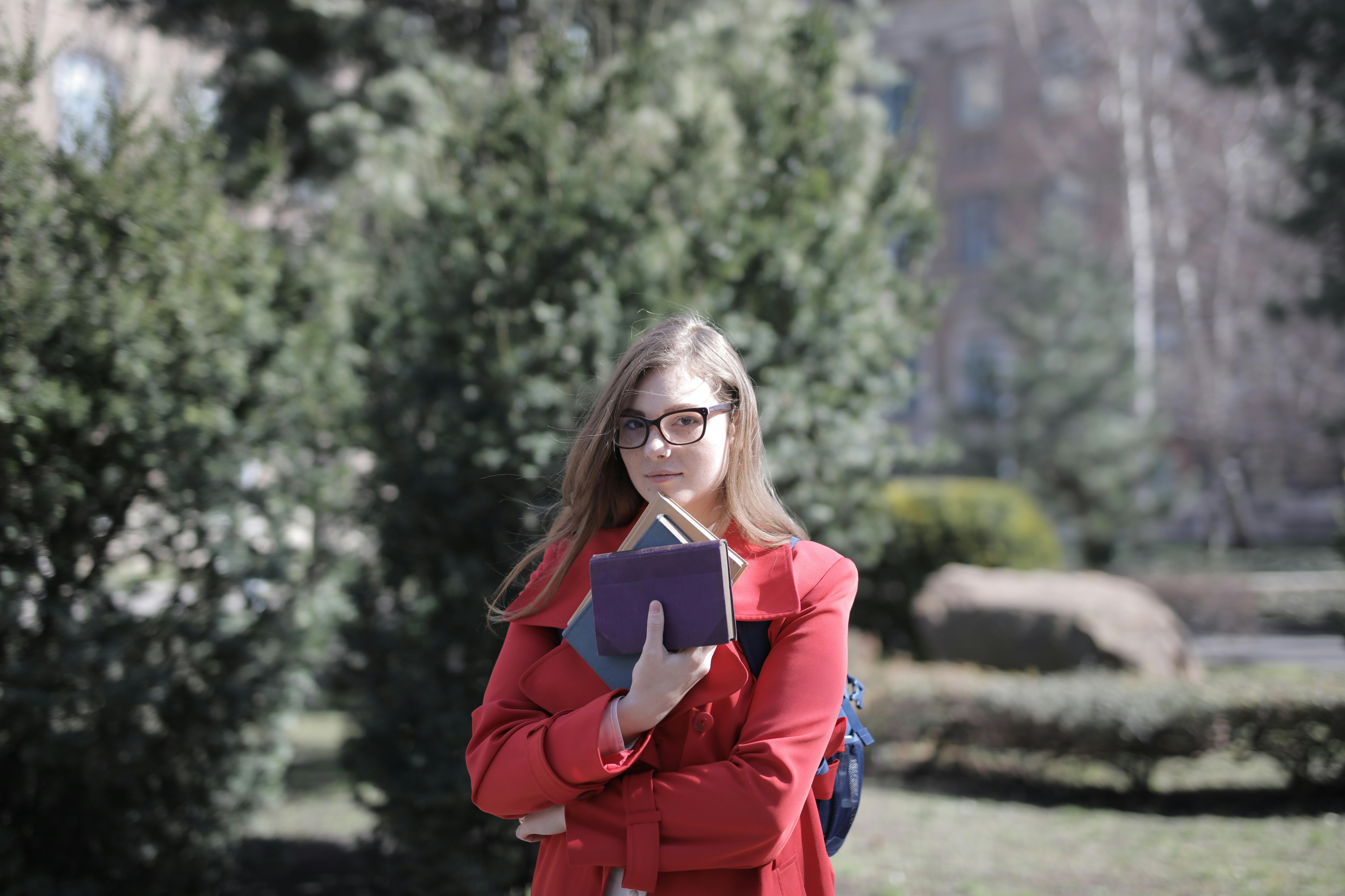 A college student stands facing the camera while smiling and holding a collection of three books.