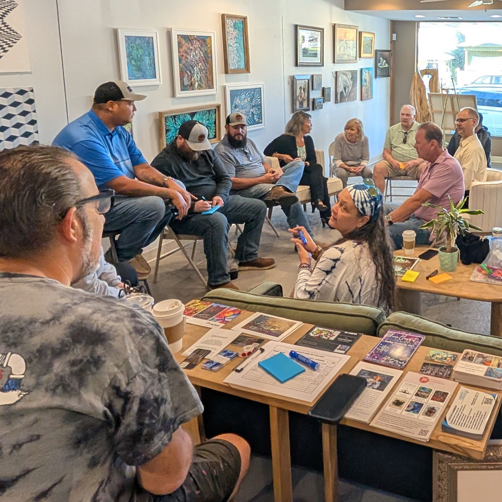 A group of workshop participants are gathered in several small groups within an art gallery space.